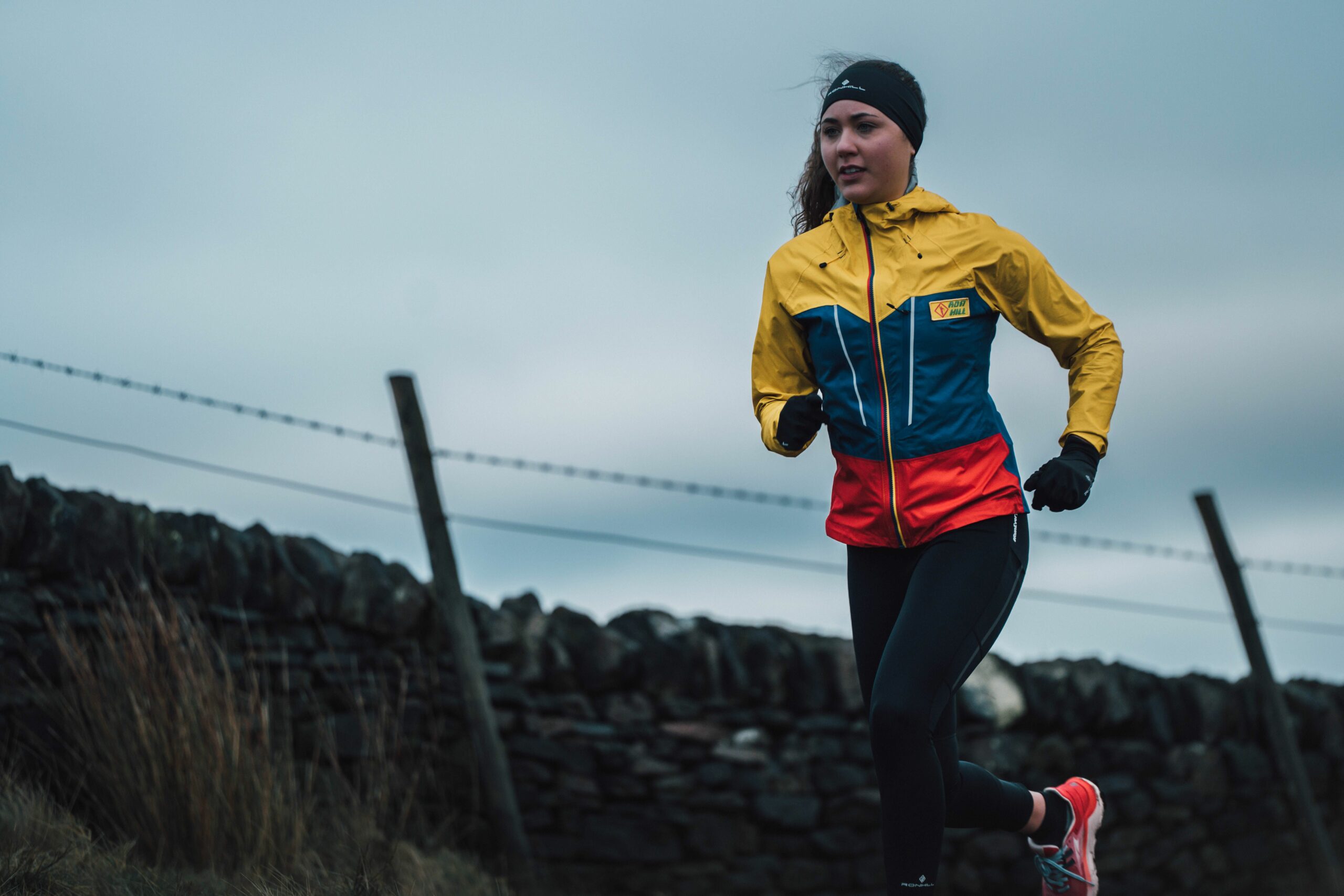 Person som løper utendørs iført en fargerik, vanntett og pustende Fortify løpejakke fra Ronhill.